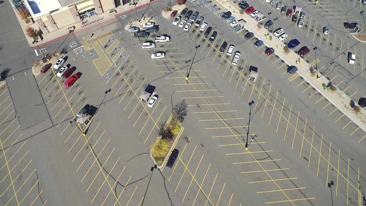 Overhead view of a mostly empty parking lot with yellow lines and a few cars.