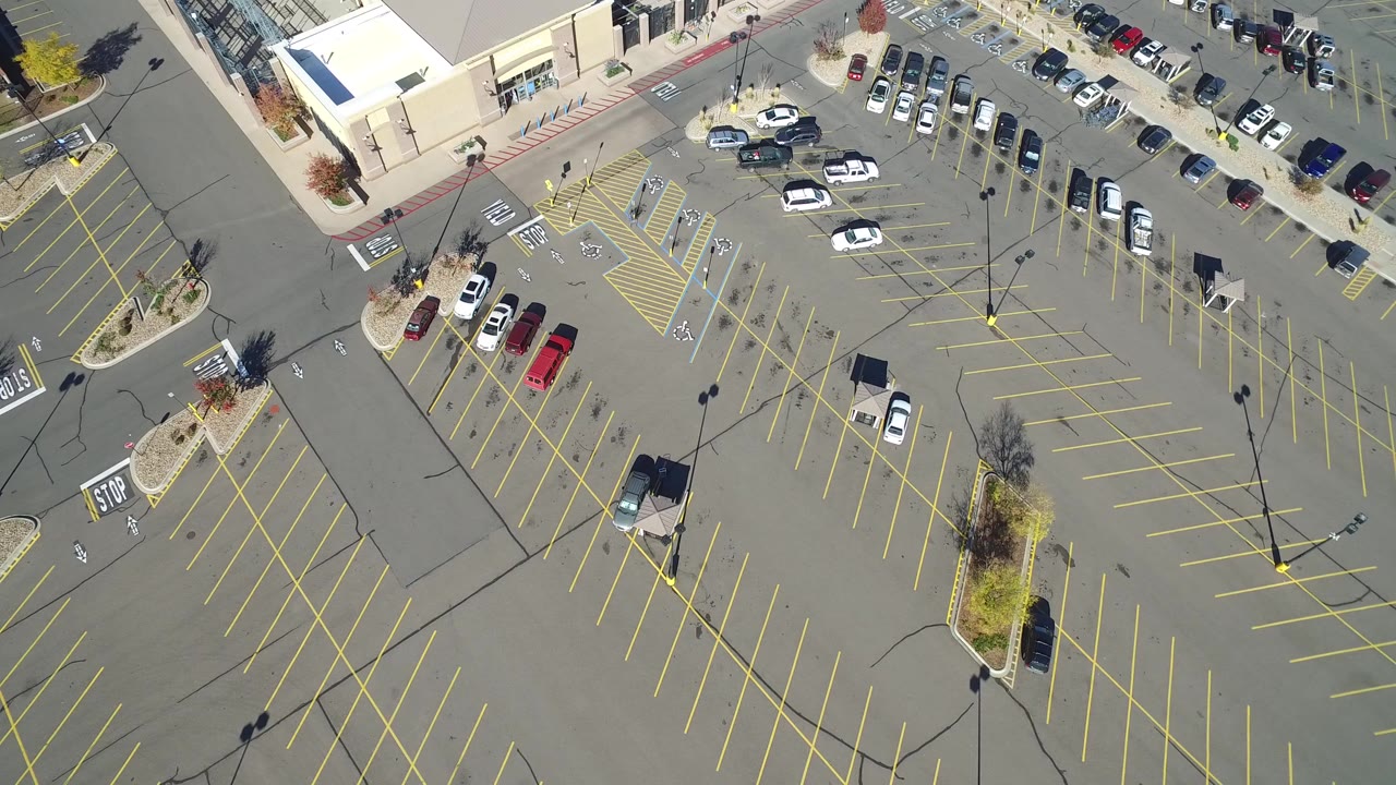 Opening frame of a Hidden Lake, Colorado parking lot seen from above, with yellow stall lines, a few parked cars, landscaped islands, and no visible people.