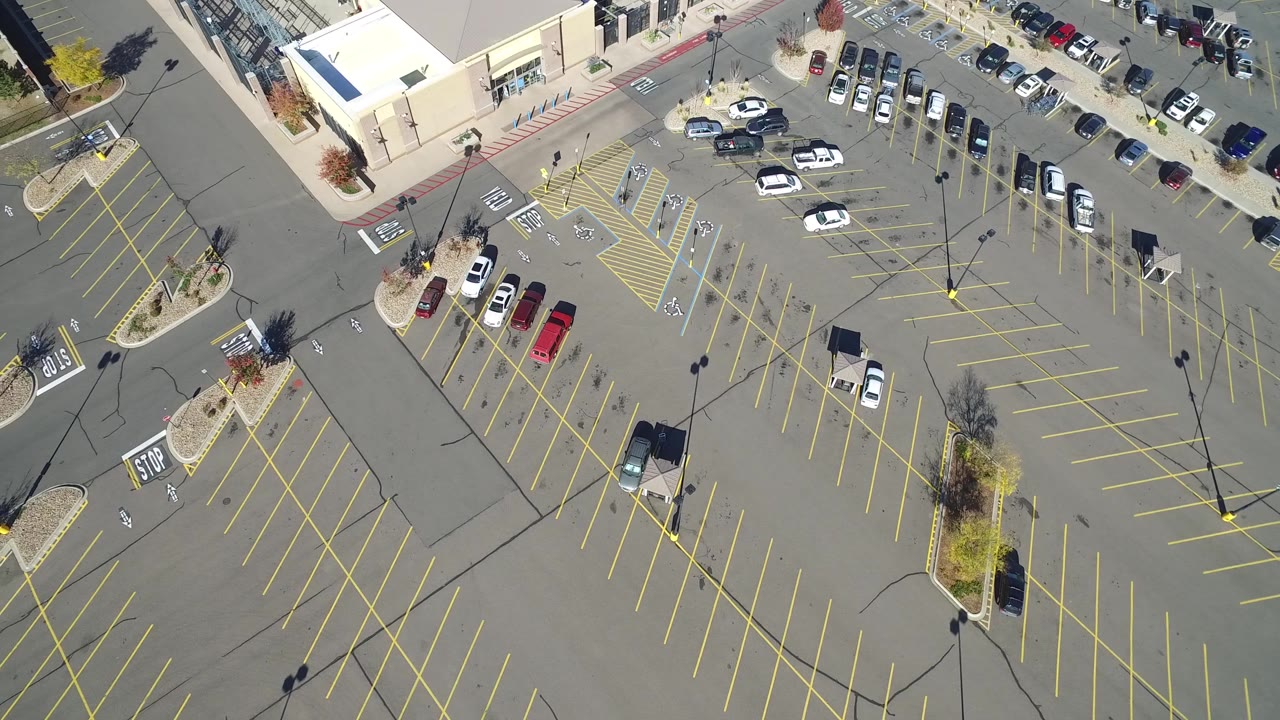 Drone-like overhead frame of open asphalt parking stalls and cars along the top edge.