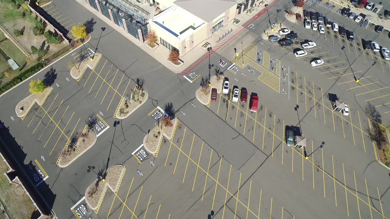 Top-down parking area with many vacant spaces, medians, and a few cars.