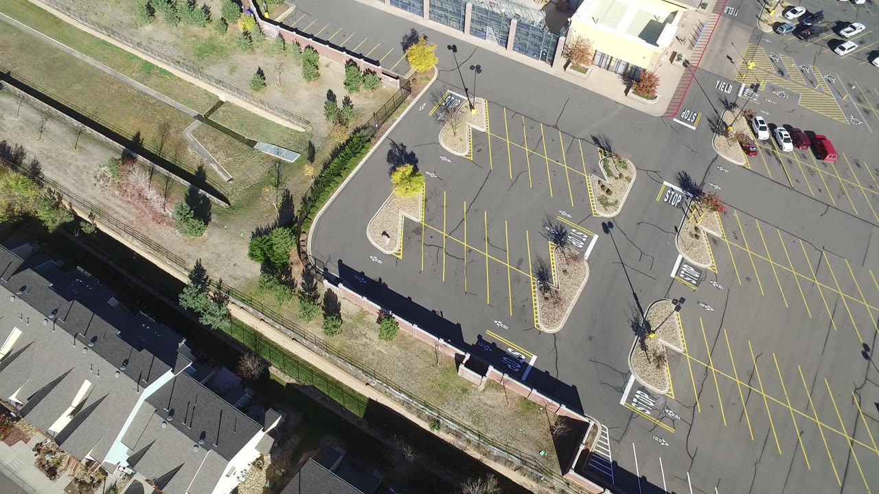 Overhead view of parking lots, homes, roads, trees, and grass.