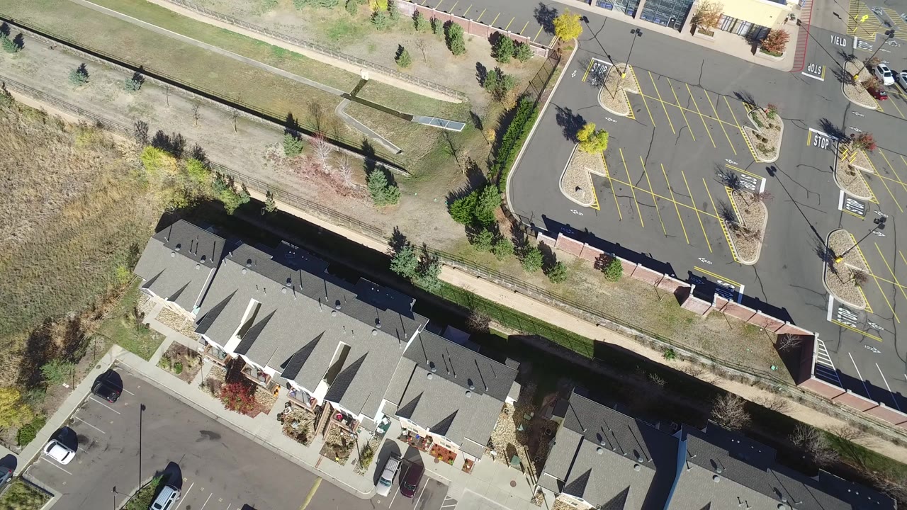 Overhead view of townhome roofs, parking lots, cars, trees, and dry open ground.