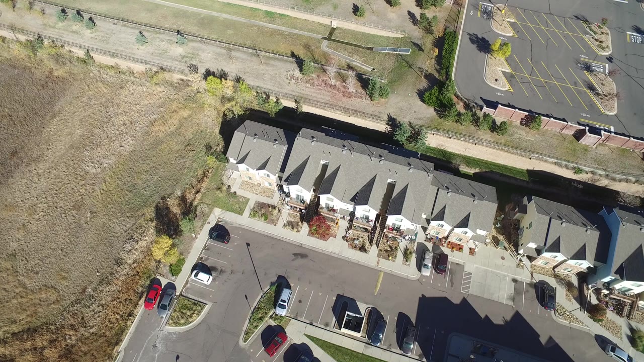 Overhead view of townhomes beside dry open land and parking areas.
