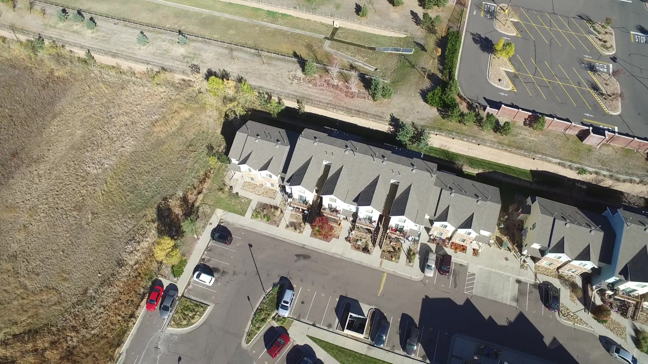 Overhead Hidden Lake, Colorado view with attached homes centered, a dry field to the left, parking spaces below, a road or path above, and no clearly identifiable people.