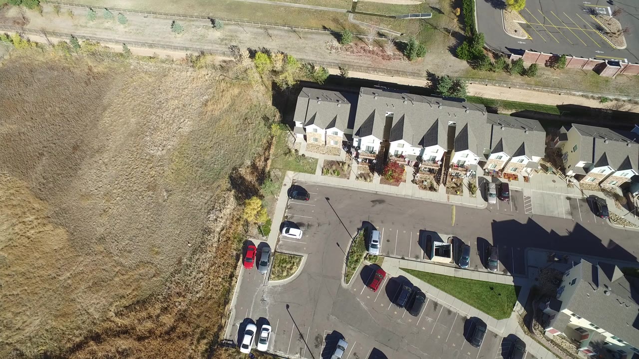 Overhead view of condos, parked cars, dry grass, and a road.