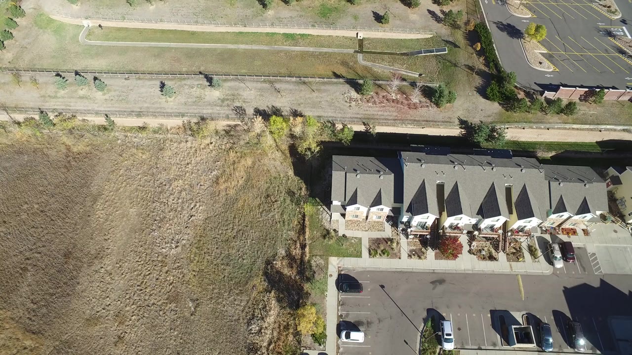 Overhead view of grass, path, parking lot, parked cars, and low buildings.