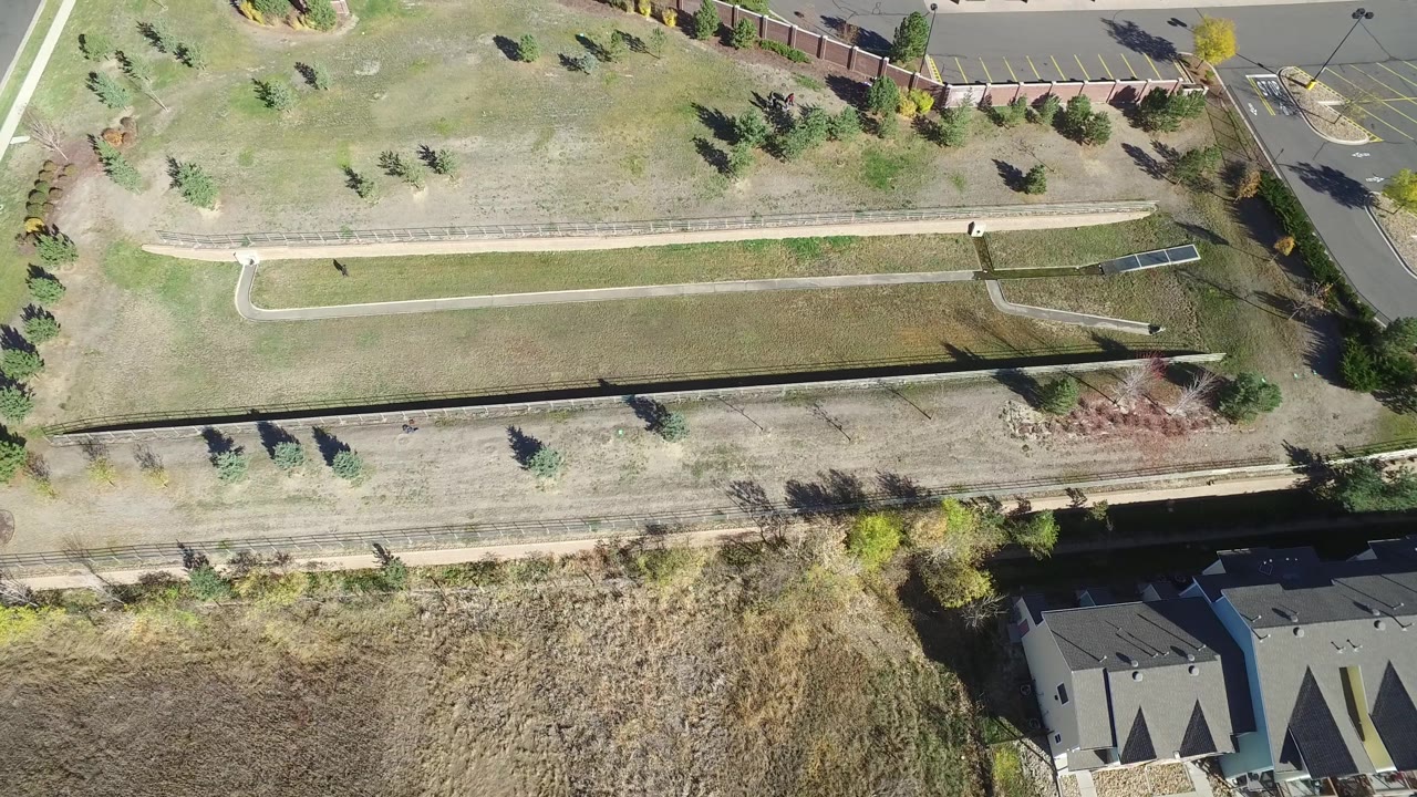 Top-down view of open land, walking paths, parking lot edge, and rooftops.