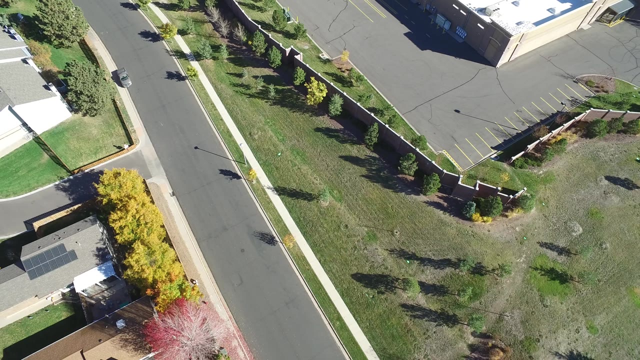 Second overhead frame in Hidden Lake, Colorado, with the road and sidewalk centered more prominently, houses along the lower edge, trees casting shadows, and a parking lot at the top.