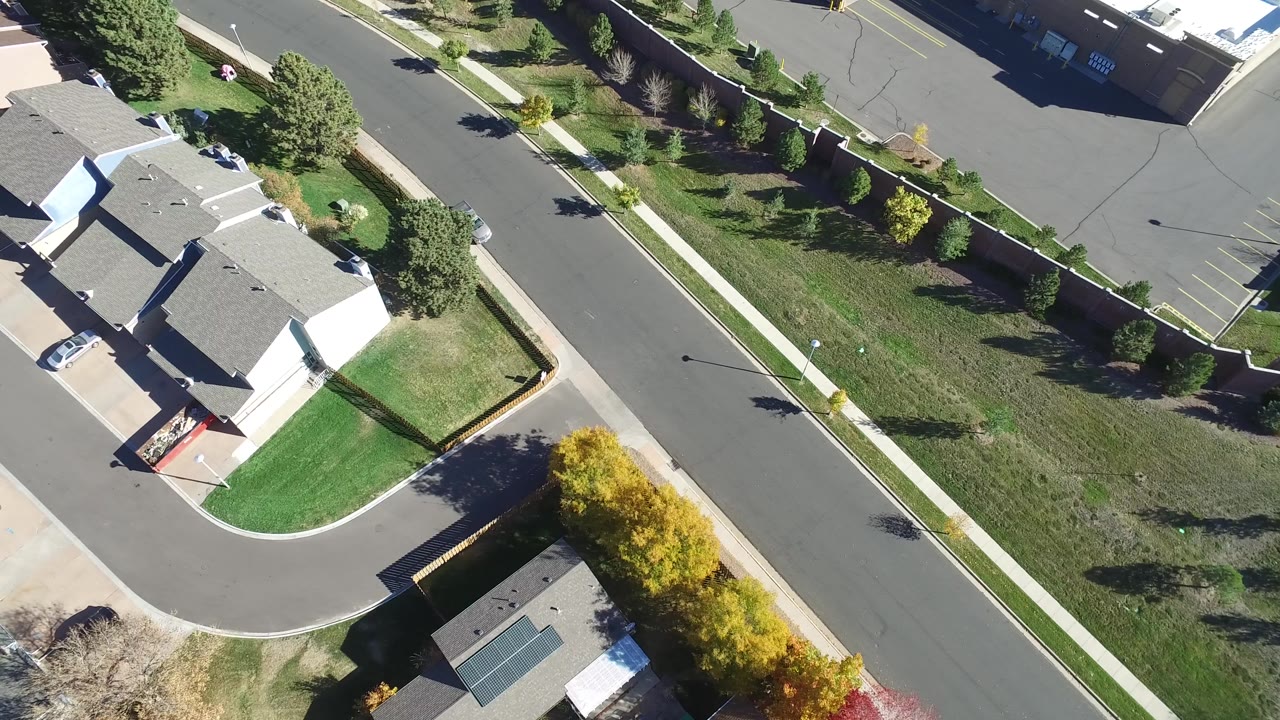 Overhead view of homes, a side street, lawns, and a parking area.