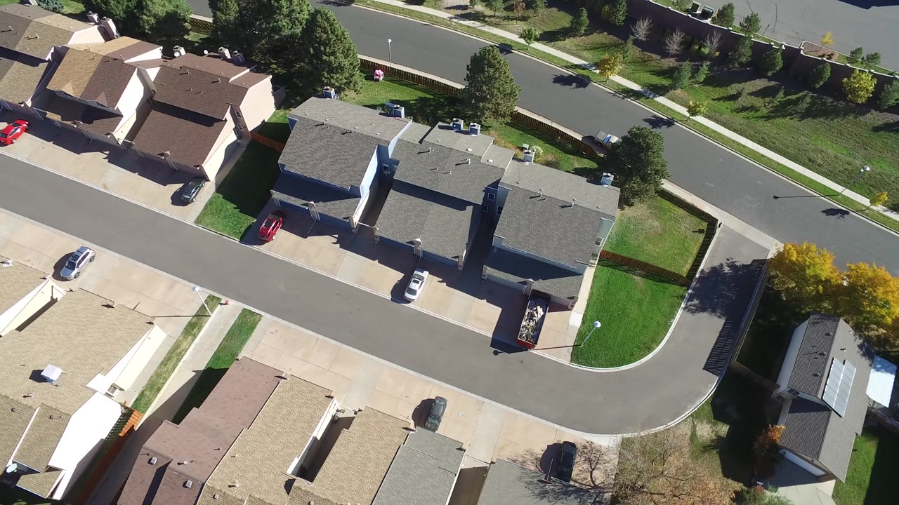 Aerial frame of Hidden Lake, Colorado showing a corner of the block with dark-roofed homes, pale driveways, lawns, trees, and no visible people.