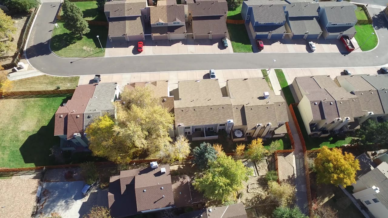 Overhead frame in Hidden Lake, Colorado showing rows of detached homes, backyard fences, yellow-green trees, a residential road, parked vehicles, and no visible people.