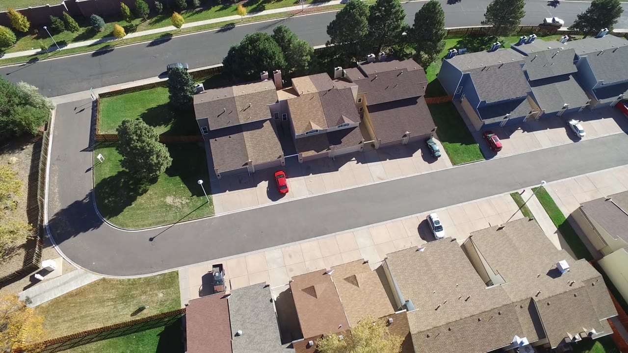 Overhead frame in Hidden Lake, Colorado showing a row of detached houses beside an asphalt street, with green lawns, sidewalks, trees, and no visible people.