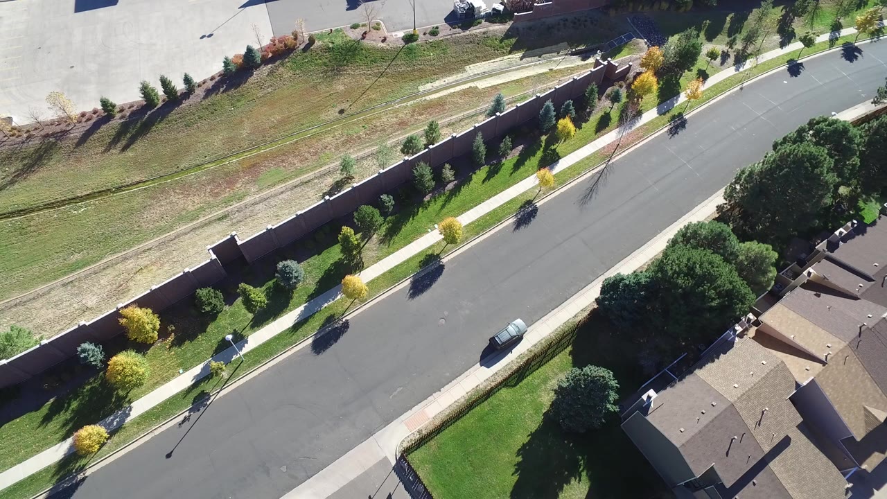 Top-down aerial view of a curved road beside lawns, trees, sidewalks, and rooftops.