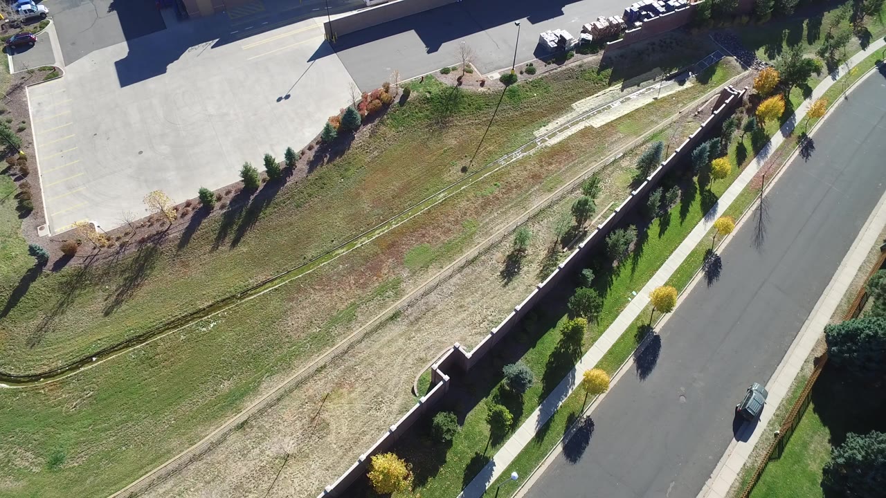 Aerial view of a parking lot, grass slope, wall, road, trees, and cars.