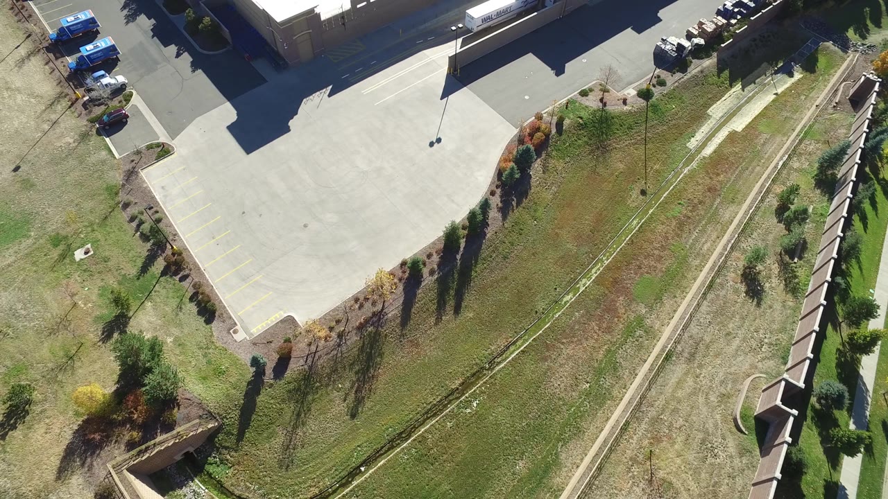 High aerial view of a building corner, parking lot, grass strip, and path.