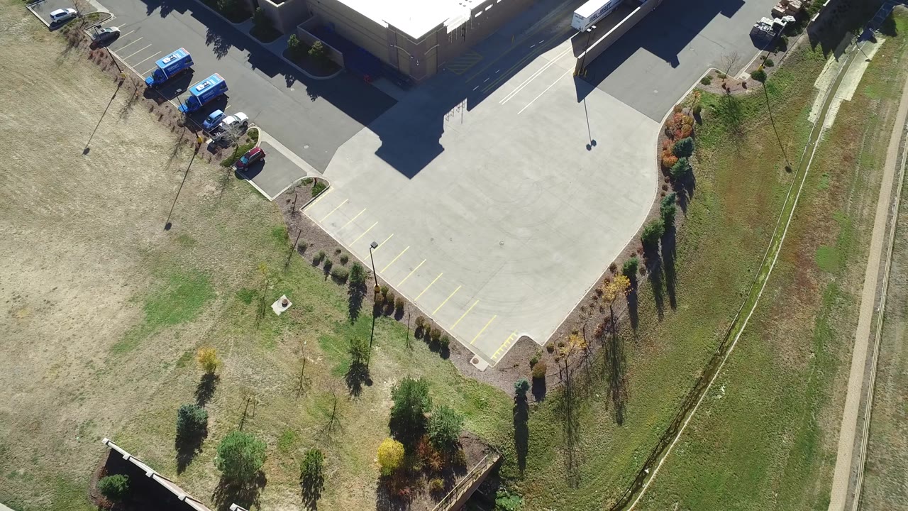 Top-down parking lot corner with blue vans, shrubs, grass, and sidewalk.