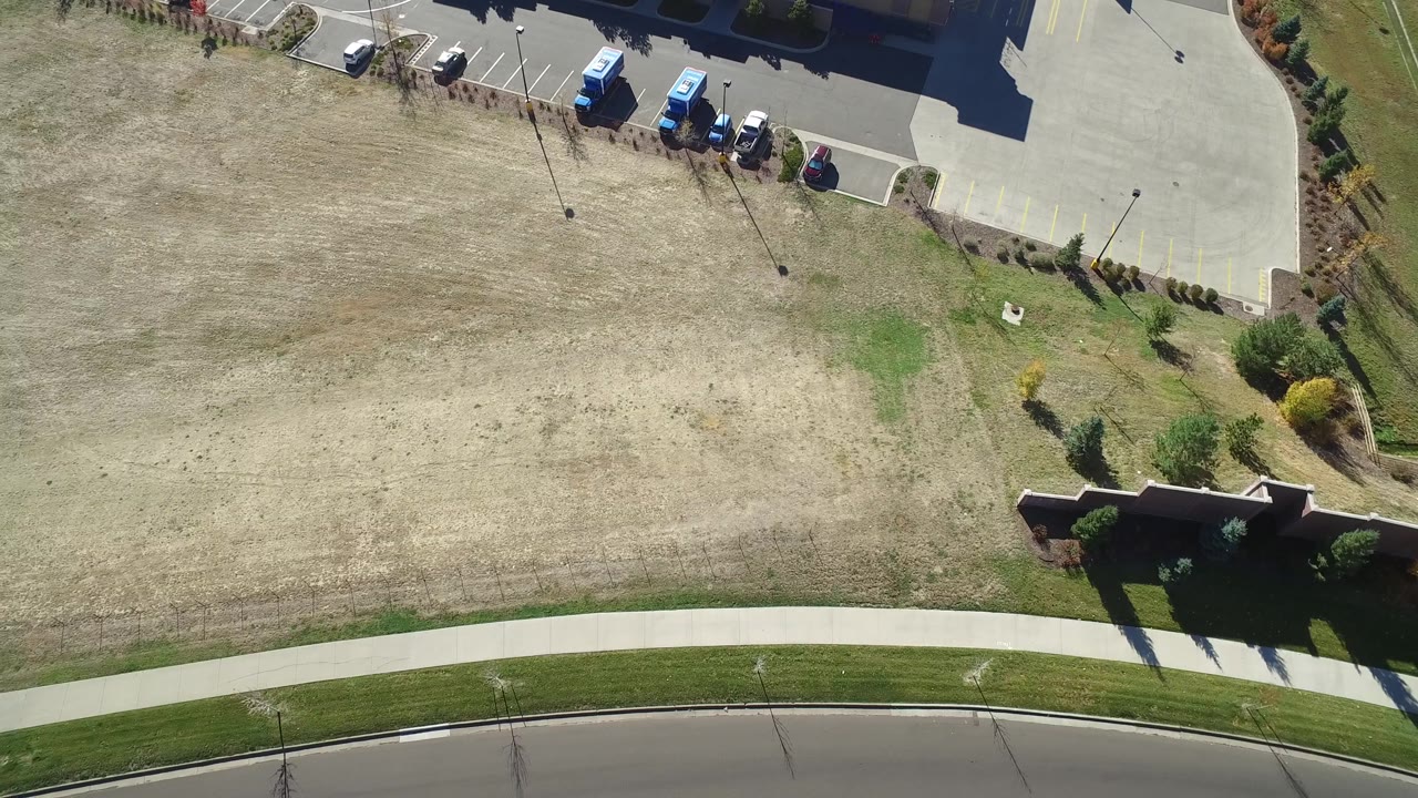 Drone-like overhead of dry field, sidewalk, road, and building corner.