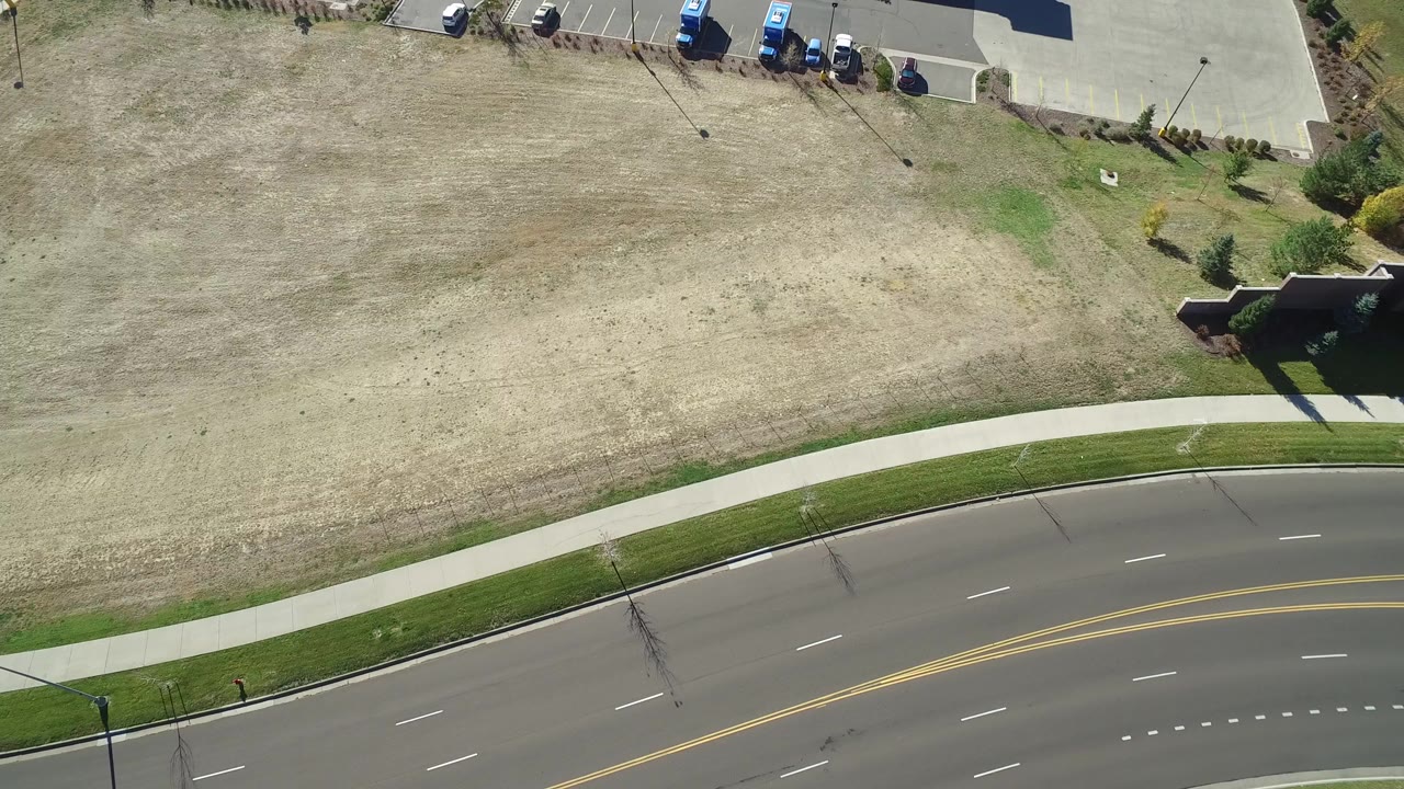 High aerial view in Hidden Lake, Colorado showing a curved divided road, sidewalk, dry open grass, parking edge, and no visible people.