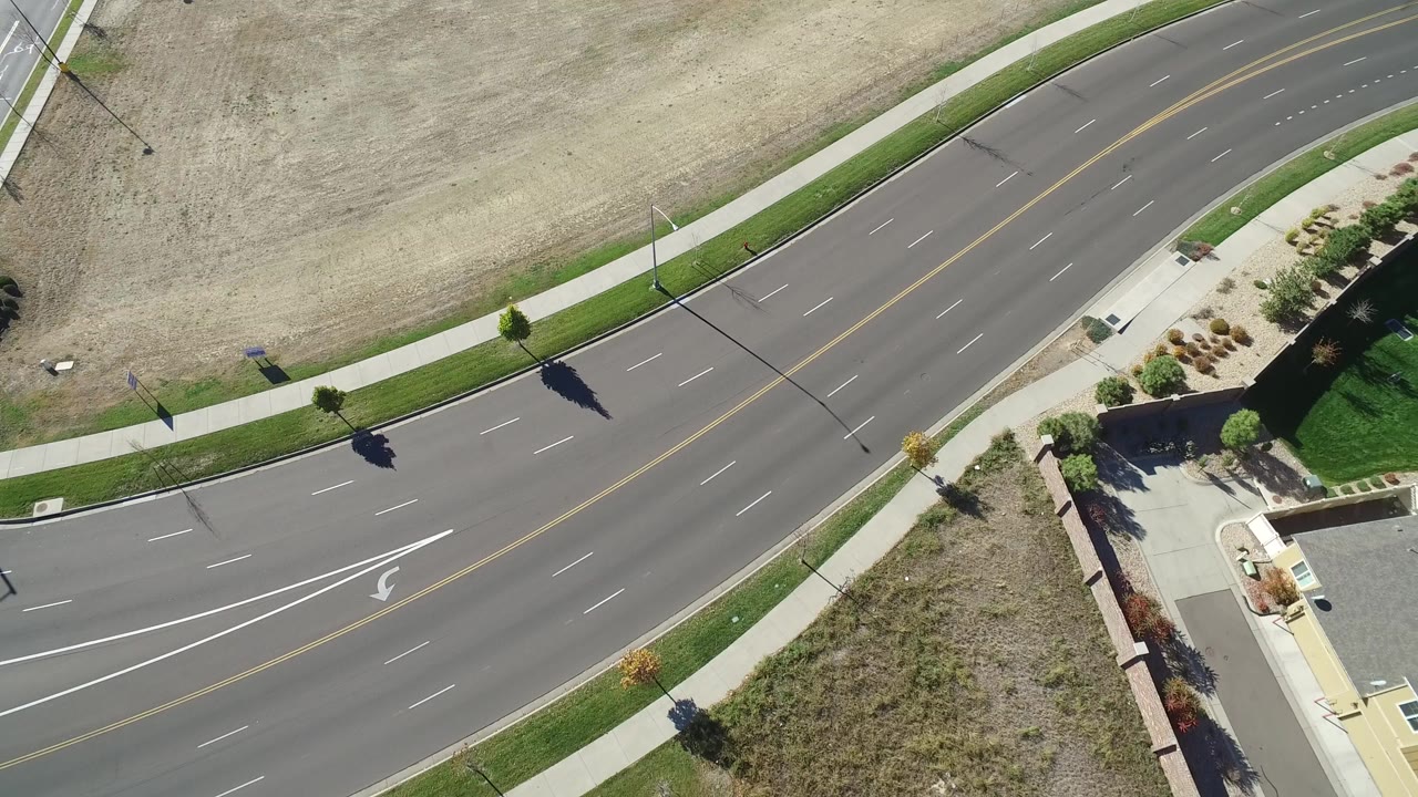 Aerial view of a curving suburban avenue beside sidewalks and dry lots.