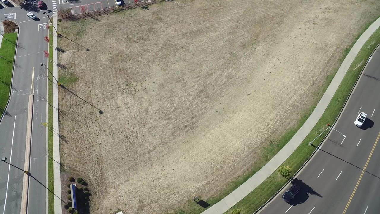 High overhead view in Hidden Lake, Colorado showing a dry grass field beside a curving black road, green verge, sidewalks, parked cars, and no visible people.