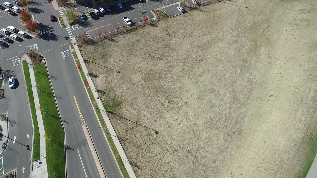 Aerial frame in Hidden Lake, Colorado with the road and narrow green median along the left, rows of parked vehicles near the top, and dry sandy ground covering the right side, with no visible people.