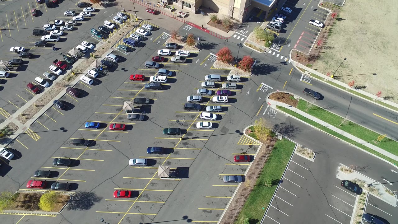 Drone view of parked cars and a road beside commercial buildings.