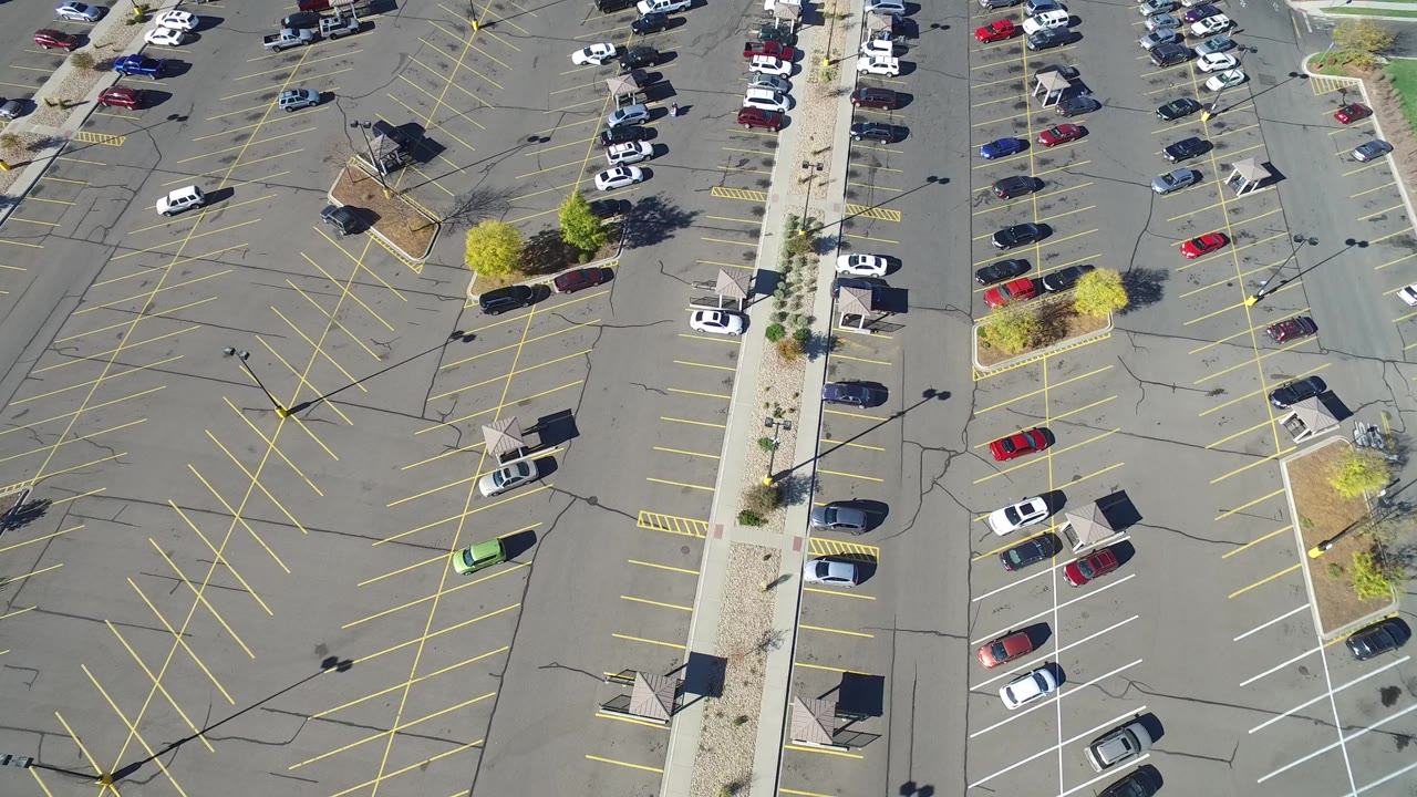 Overhead view of a mostly empty parking lot with marked spaces and scattered cars.