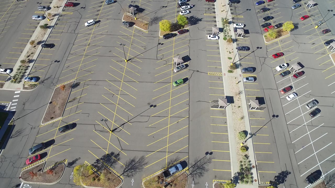 Overhead view of a mostly empty parking lot with landscaped islands and a few cars.