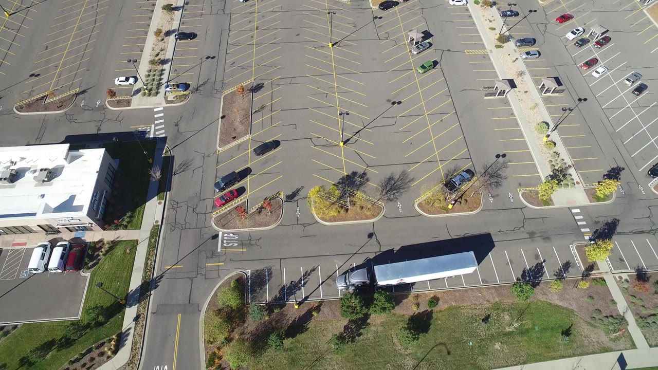 Top view of a commercial building, empty parking spaces, roads, grass, and trees.