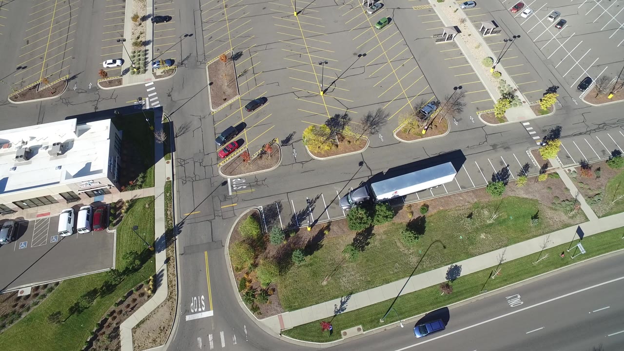 Overhead view in Hidden Lake, Colorado with a blue car on the road, rows of marked parking spaces, building roofs, sidewalks, and no visible people.
