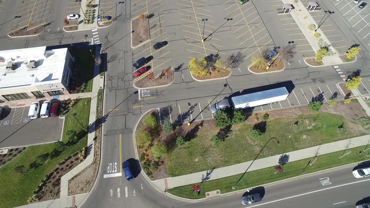 Overhead view of a truck and trailer parked across spaces beside a road and building.