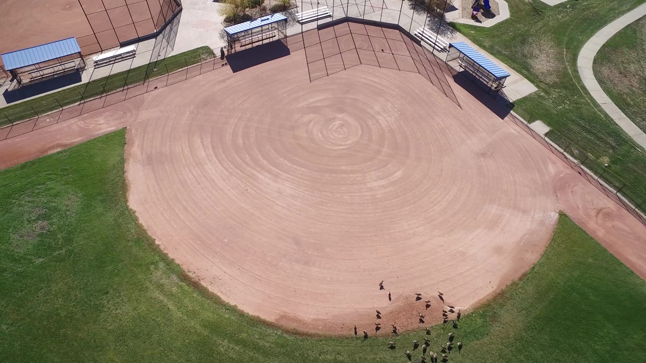 Aerial view of the Hidden Lake, Colorado ballfield with circular rake patterns in the infield and a cluster of small people along the lower right grass line.
