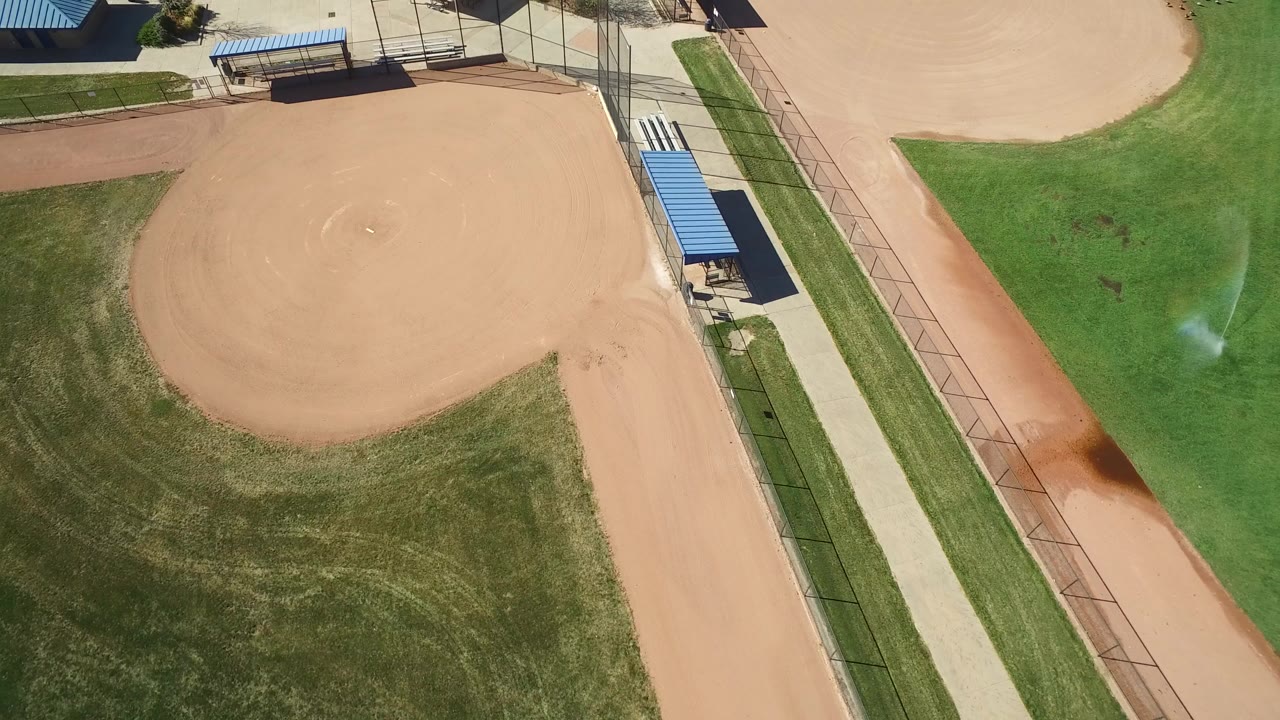 High aerial frame over a Hidden Lake, Colorado baseball field, showing the tan infield, green outfield, paths, fencing, blue-roofed dugouts or shade structures, and no visible people.