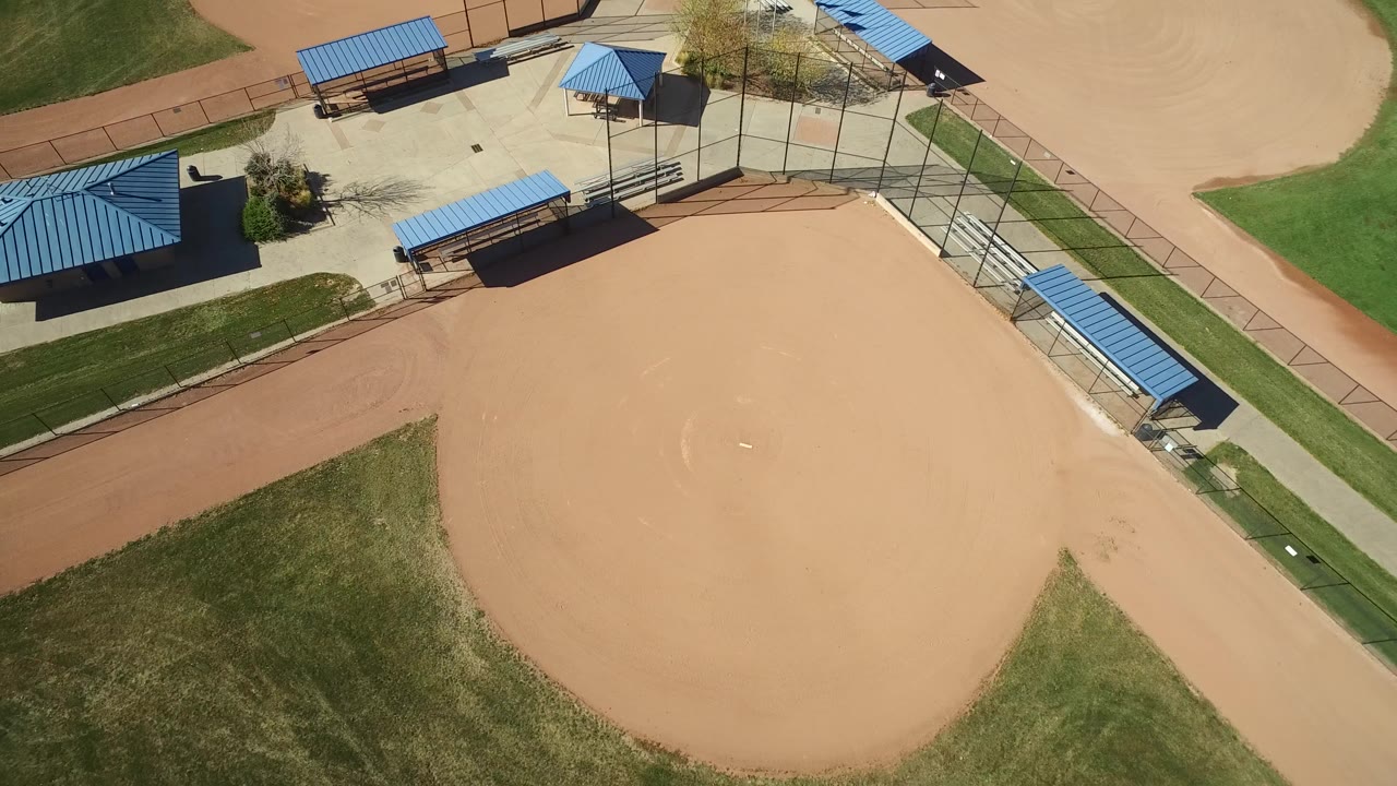Overhead view of an empty baseball infield and blue-roofed park shelters.