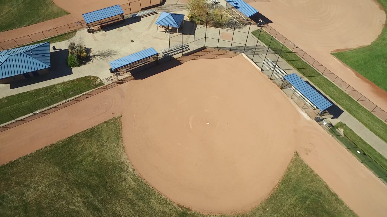Aerial frame in Hidden Lake, Colorado with the infield shifted slightly lower in view, bordered by green grass, a paved path, blue shelters, fencing, and no visible people.