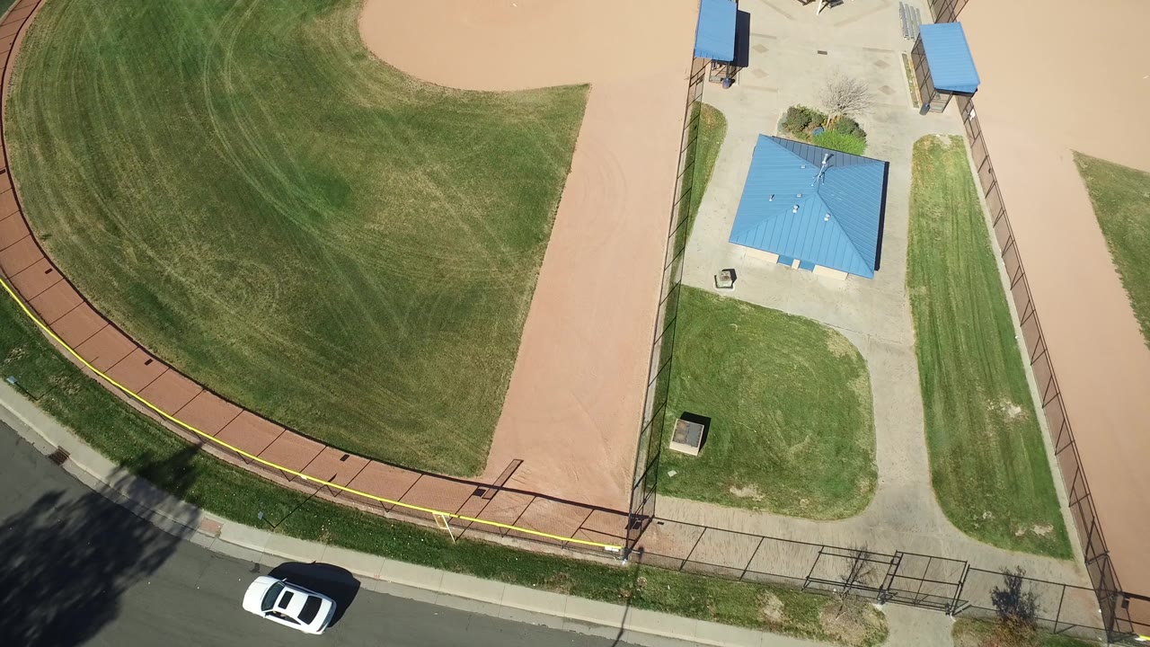 Aerial view of green outfield, tan infield, park shelters, fencing, and road.