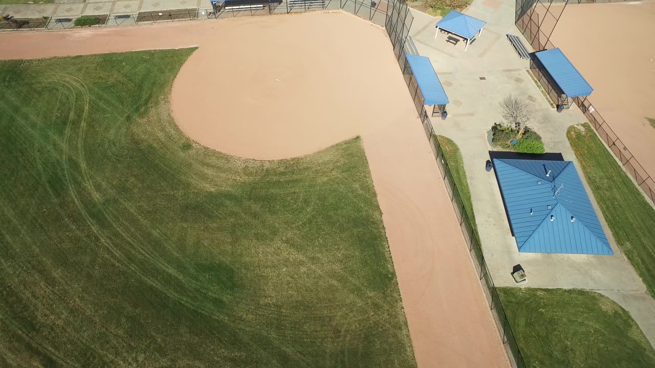 Overhead view of an empty baseball field and blue-roofed park structures.