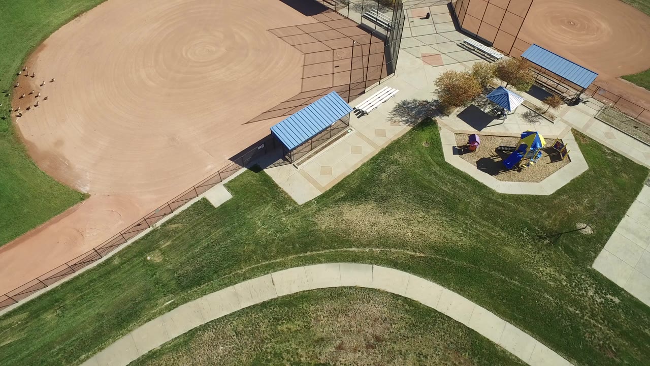 Overhead view of a ballfield edge, playground, grass, and curved path.