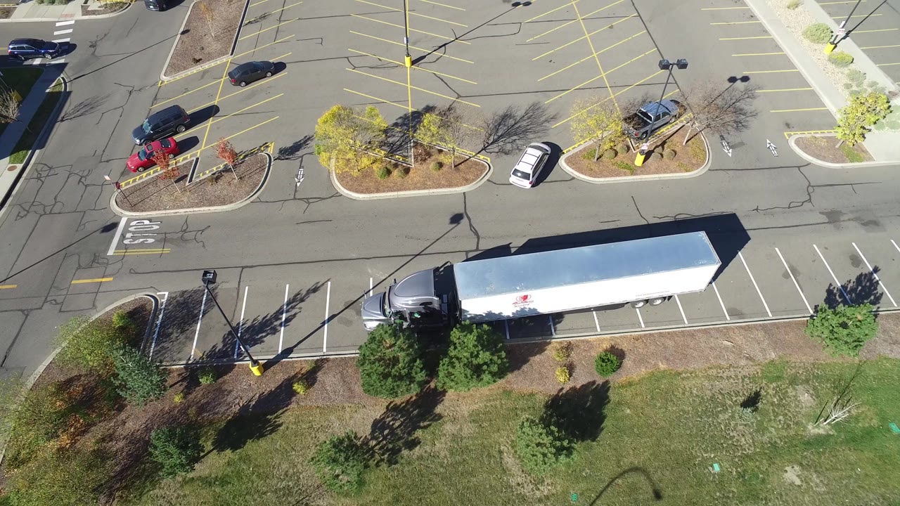 Drone view of mostly empty parking spaces with cars, islands, and trailer edge.