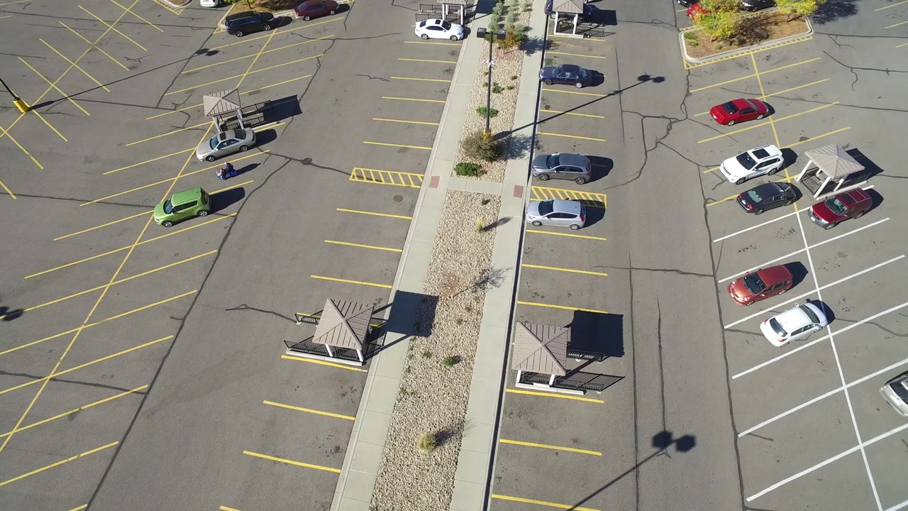 Top-down parking area with empty spaces, a red car, white cars, and median landscaping.