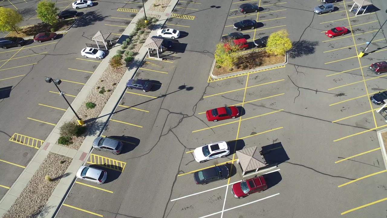 Aerial view of a partially full parking lot with yellow lines and scattered cars.