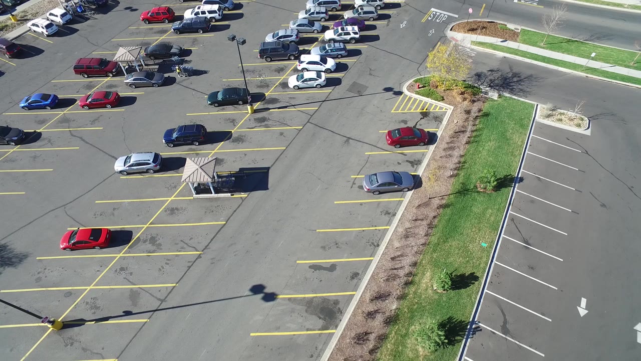 High aerial view of a Hidden Lake, Colorado parking lot with scattered parked cars, yellow stall lines, a landscaped grass strip, sidewalks, and no visible people.