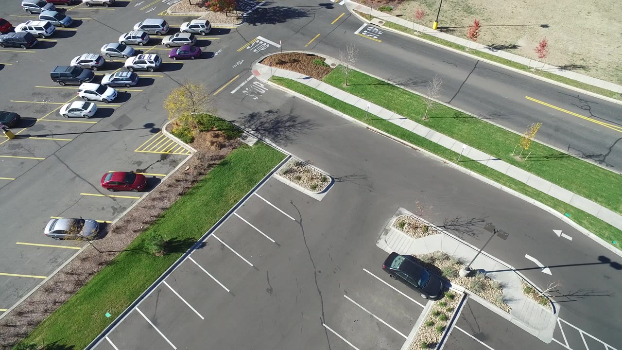 Aerial frame in Hidden Lake, Colorado showing parked cars at the upper left, a clean road across the top, parking lanes below, green grass strips, and no visible people.