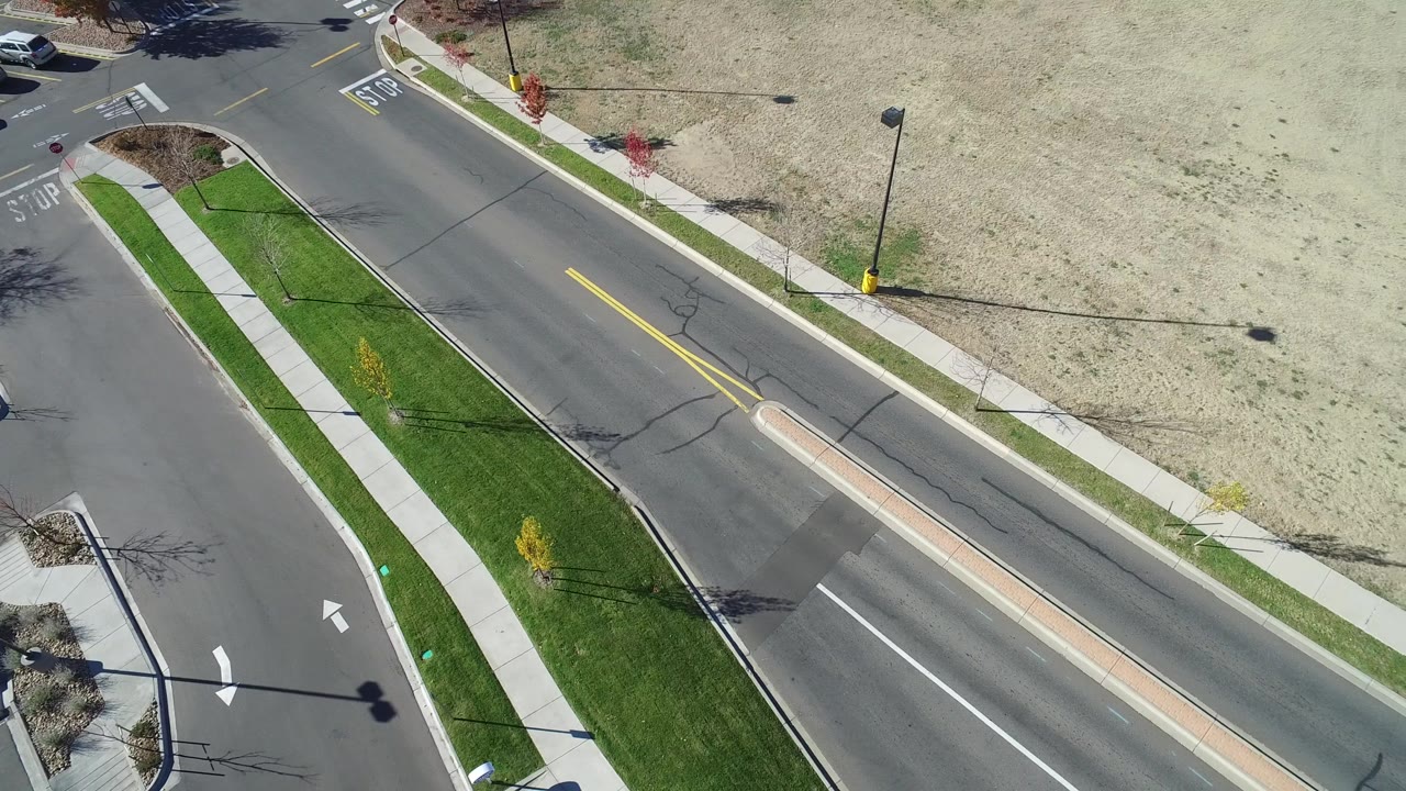 Aerial road view with a sidewalk, grass strip, and open field.