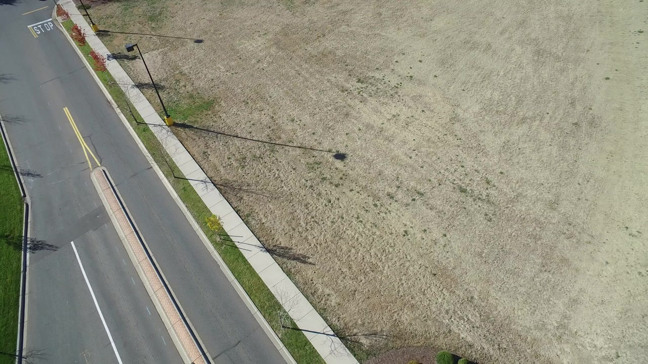 High aerial view over Hidden Lake, Colorado showing tan grassland, a paved road, a narrow sidewalk, streetlights, and no visible people at the start of the clip.