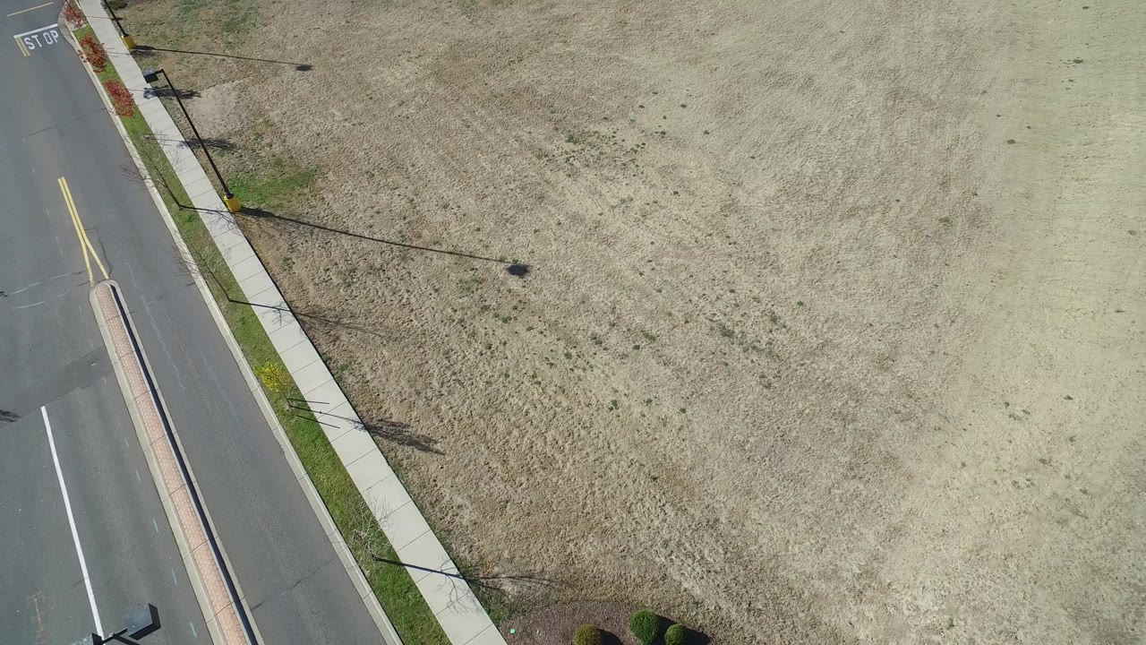 Aerial view of an open field beside a road, curb, and sidewalk.