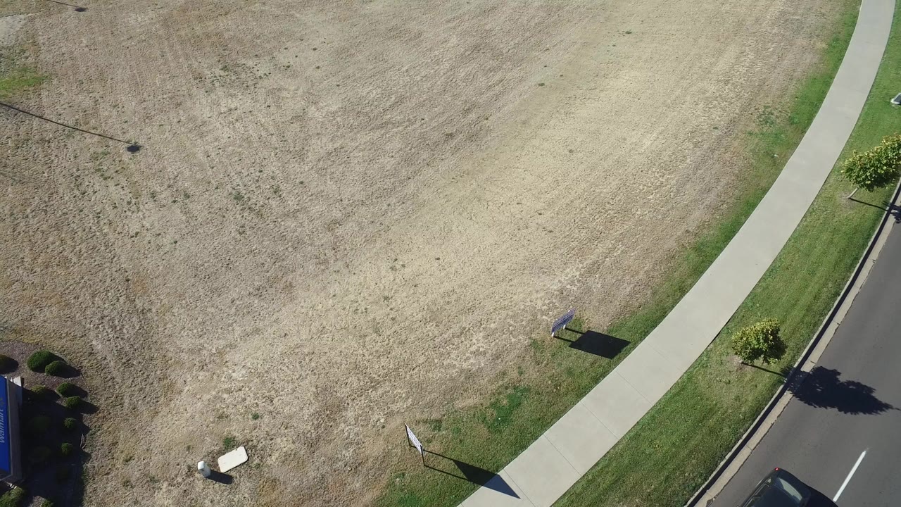 Opening overhead frame in Hidden Lake, Colorado showing a dry field, curved sidewalk, strip of green grass, road edge, small signs, and no visible people.
