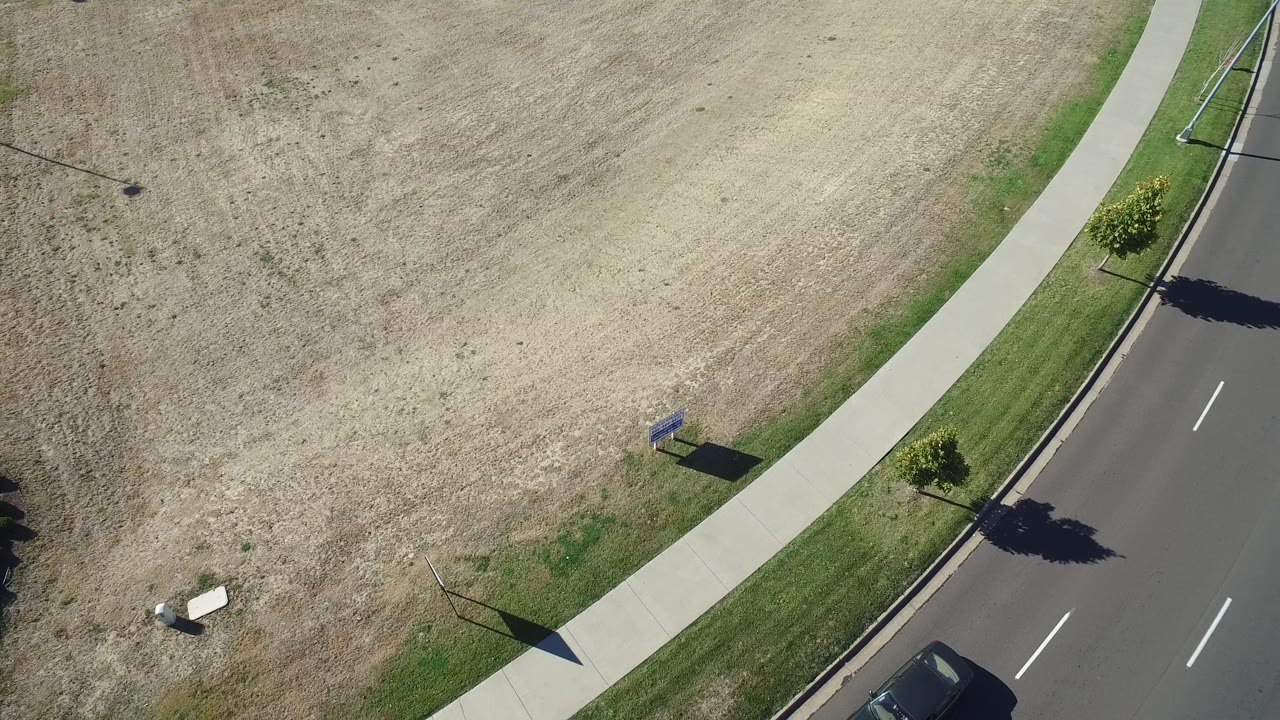 High angle view of divided road, sidewalk, field, and a car near the lower edge.