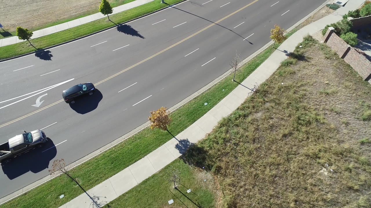 Dark car and pickup truck traveling on a suburban road seen from above.