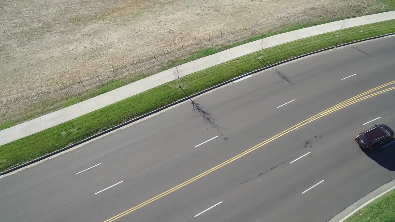 Overhead road beside sidewalk and grass with a dark car near the right edge.